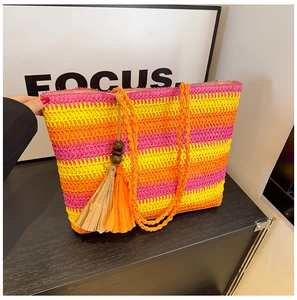 Detail of colorful woven straw tote bag with vibrant pink orange stripes and tassel charm