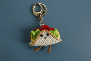 Macro shot of handmade crochet taco keychain with metal clasp on blue background