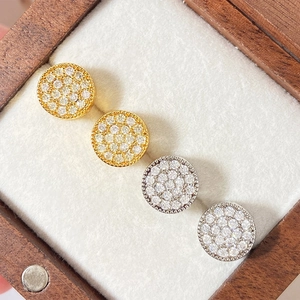 Detailed close-up of gold and silver round stud earrings with pave-set crystals in a wooden box