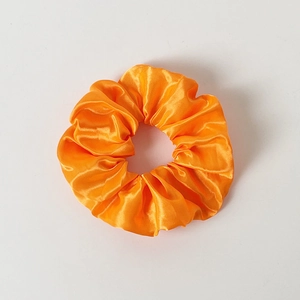 Close-up of bright orange satin LED hair scrunchie showing smooth fabric texture and glow