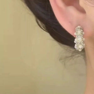 Macro close-up of gold-plated pearl and rhinestone stud earrings on woman's earlobe