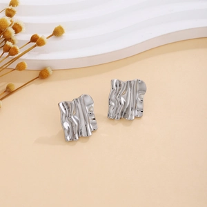 Macro detail of silver geometric liquid metal earrings on a beige wavy display