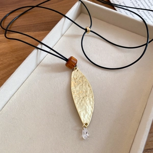 Macro shot of leaf pendant with brown resin bead and crystal drop on black leather cord