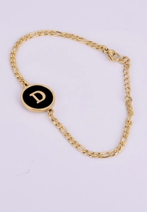 Detail of 18K gold Figaro chain bracelet with a black and gold letter D shell charm