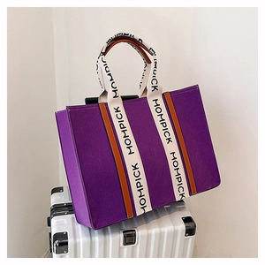 Detail of a large purple felt tote bag with MOMPICK branded straps on a silver suitcase
