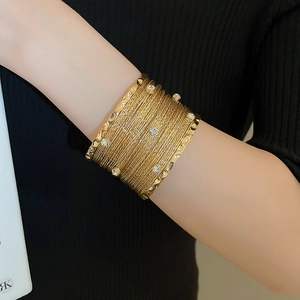 Macro detail of multi-layer gold cuff bracelet with sparkling crystal stones on woman arm