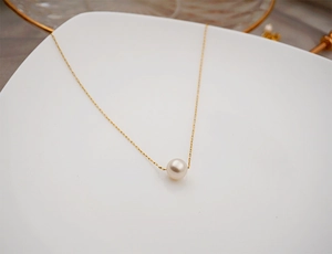 Close-up of a single white pearl pendant on a thin gold chain resting on a white plate