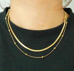Detail of layered gold snake chain and beaded necklace on woman's neck