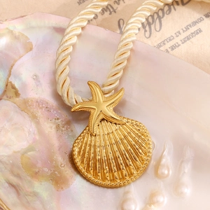 Close-up of 18K gold starfish shell pendant on a woven cord necklace with beach props