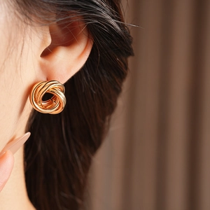 Gros plan de boucles d'oreilles nœuds torsadés dorés sur un modèle montrant le design moderne