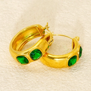 Macro detail of gold-plated hoop earrings featuring three square green crystal stones