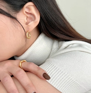 Detail of twisted gold knot earrings and ring set worn on model with elegant styling