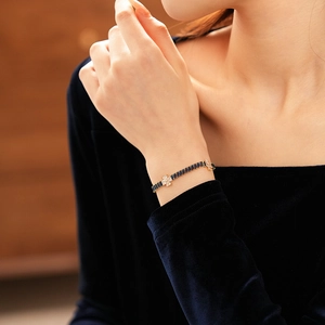 Detail of luxury gold bracelet with navy blue stones and zircon clover on woman's wrist