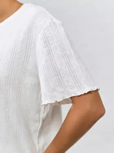 Detailed macro view of white cotton knit top featuring eyelet pattern and lettuce edge sleeves