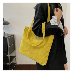 Detail of a bright yellow corduroy tote bag with fashion label on black blazer background