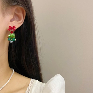Close-up of handmade beaded Christmas tree earrings with a red bow on model