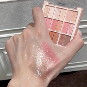 Close-up of 18-color eyeshadow palette with pink matte and glitter swatches on arm