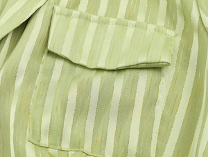 Close-up of green striped utility dress fabric with metallic thread and flap pocket detail