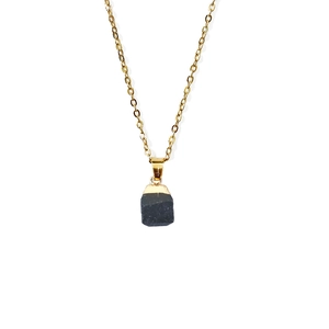 Detail of a natural black raw stone pendant with gold-plated edge on a thin golden chain