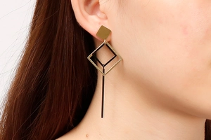 Detail of geometric rhombus drop earrings with gold and black frames worn by model