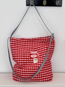 Red plaid woolen tote bag with cherry patch and gray strap hanging on a hook