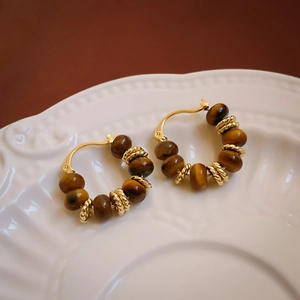 Detailed macro of gold tiger eye beaded earrings on an elegant white ceramic dish