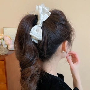 Detail of a white satin bow hair clip with black polka dots on a high ponytail