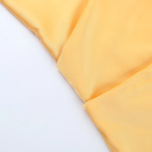 Détail du tissu en satin jaune brillant montrant une texture lisse et un drapé élégant