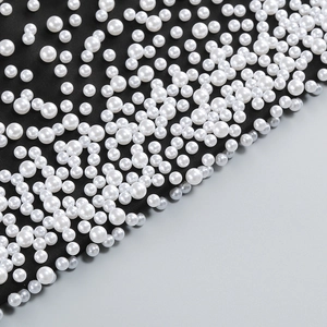 Detailed macro shot of white faux pearls hand-stitched on black fabric for an elegant evening gown