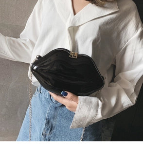 Detail of a chic black glossy lip-shaped crossbody bag with gold chain strap on a model