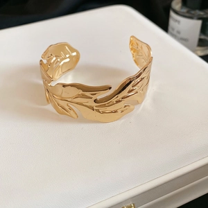 Macro shot of gold leaf-shaped open bracelet with detailed veins on a white leather stand
