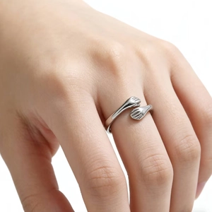 Macro detail of silver hugging hands ring featuring polished metallic finish on finger