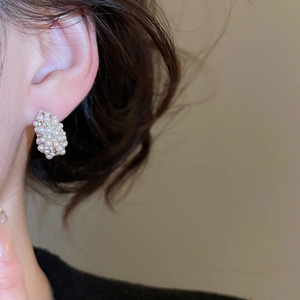 Close-up of elegant C-shaped pearl earrings with zircons worn on a model's ear