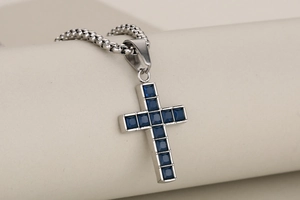 Detailed view of silver cross pendant with square-cut blue crystals on a box chain