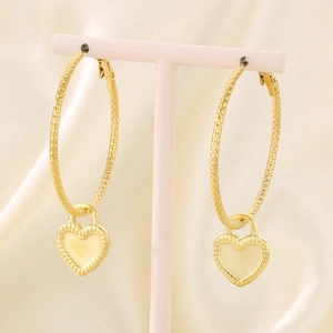 Detail of golden hoop earrings with heart-shaped pendant on silk background