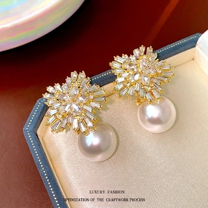 Sparkling crystal flower earrings with large white round pearl drops on silk background