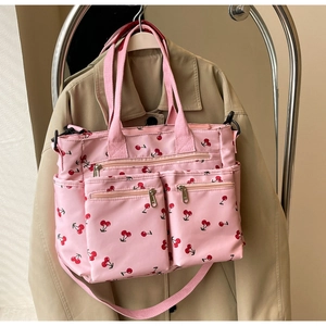 Pink tote bag with cherry print and multiple zipper pockets on beige trench coat background