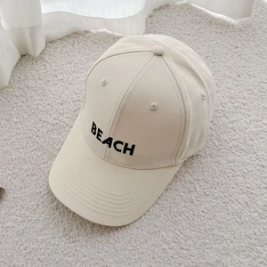 Macro detail of black BEACH letter embroidery on off-white cotton baseball cap