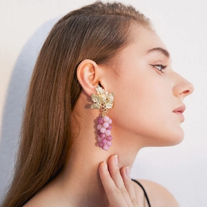 Close-up of model wearing purple grape earrings with golden leaf details and beads