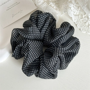 Detail showing high-elasticity black polka dot mesh hair scrunchie on white lace background