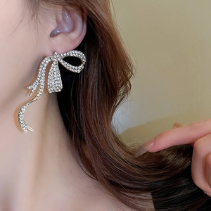 Détail macro de boucles d'oreilles nœud argentées avec strass brillants et pompons