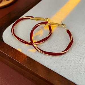 Detailed view of twisted gold-plated metal earrings with dark red enamel finish