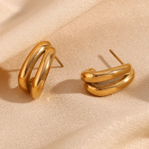 Macro shot of minimalist gold double-layer curved stud earrings on champagne silk fabric