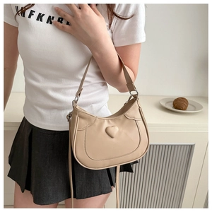 Detail of beige saddle bag with heart decoration and adjustable strap on model