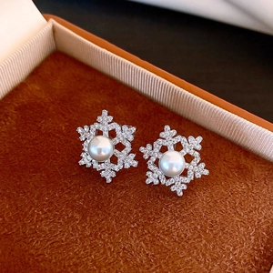Macro view of silver snowflake stud earrings with white pearl and sparkling zircons