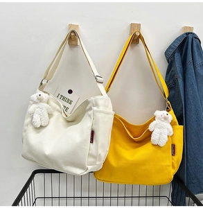 Detailed shot of white and yellow canvas bags with plush bear charms hanging on hooks