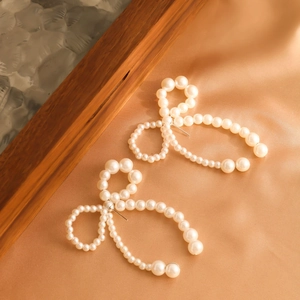 Elegant bow-shaped earrings made of imitation pearls on a champagne satin background