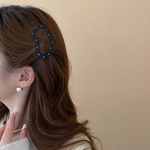 Close-up of black hair clip with white polka dots and pearl earrings on a model