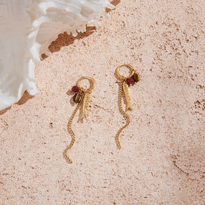 Close-up of 18K gold fish pendant earrings with tassels and tiger eye beads on sand