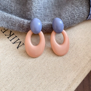 Close-up of lilac and peach acrylic oval geometric earrings on a woven fabric background